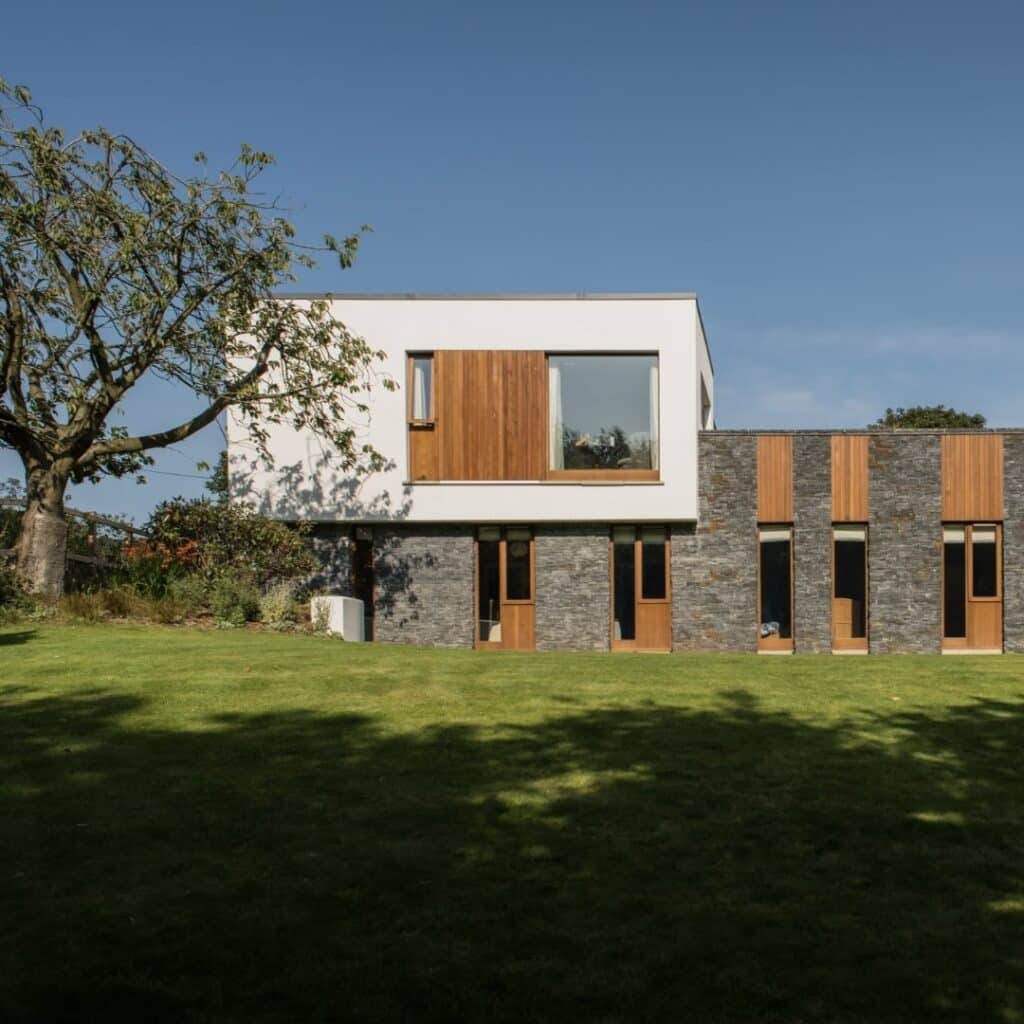 A modernist home with a grass garden in front and a tree to the left 