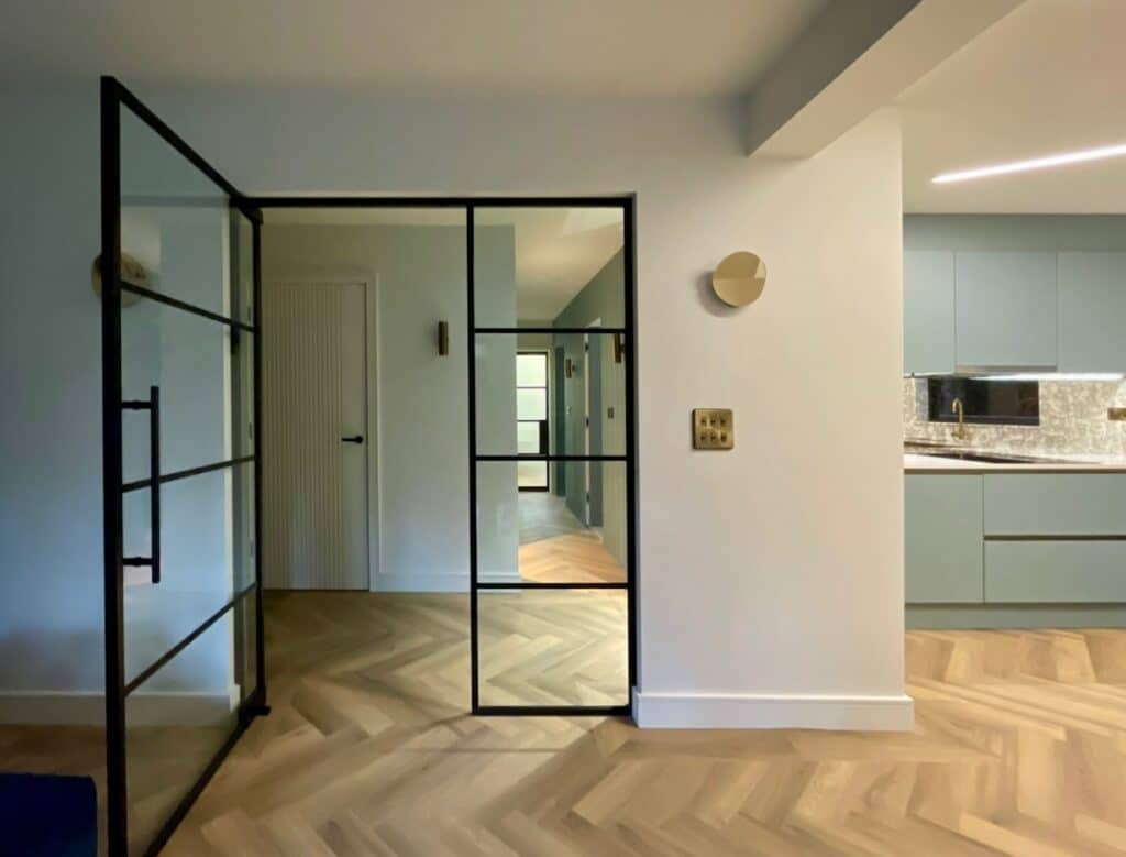 Interior open living and kitchen space opening into an entrance hallway through internal steel glazing